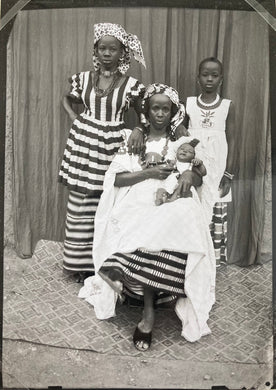 Seydou Keita - A mother seated with her child in her arms in a white boubou and loincloth and a woman standing in a bayo fabric dress